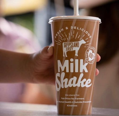 Hand holding a Gippsland Jersey milkshake cup with branding and text.